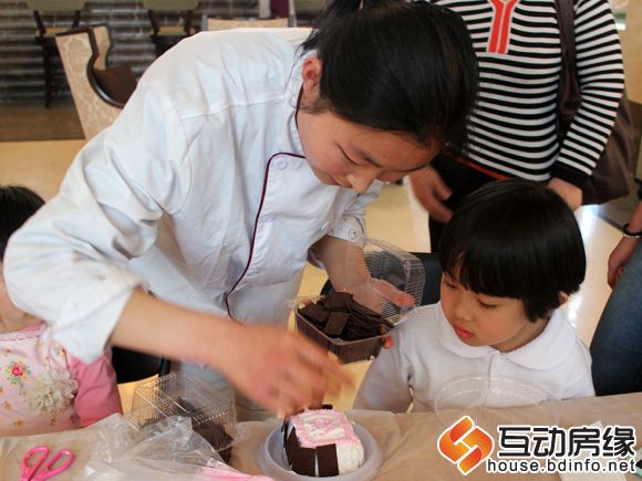 图为烘焙师帮助小朋友在蛋糕上贴上巧克力片