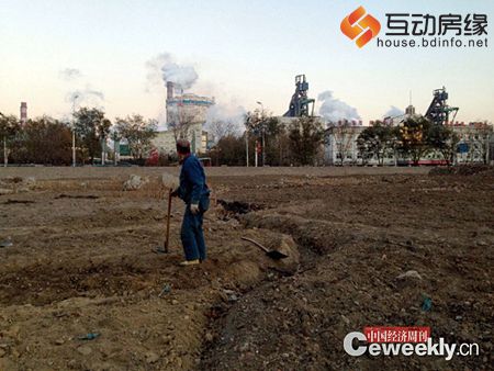 河北省唐山市丰南区，移民农民在一块荒地上耕作，他身后是一墙之隔的钢铁生产车间。